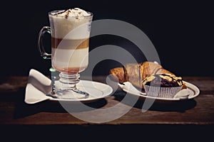 Glass of Latte macchiato with rich milk foam. Hot chocolate and coffee beverage with whipped cream and sweet cupcake and croissant