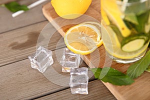 A glass of lemon cucumber water and fresh lemon fruit, ice cubes and mint leaves on a cutting board