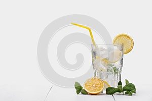 Glass of lemon drink with fresh lemons, mint and ice cubes on light wooden table cope space