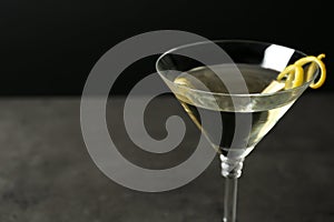 Glass of lemon drop martini cocktail with zest on stone table against black background, closeup.