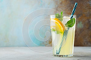 Glass with lemonade or mojito cocktail with lemon and mint, cold refreshing drink or beverage with ice on rustic blue background.