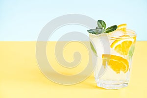 Glass with lemonade with orange, mint and ice over yellow background with copy space