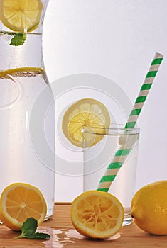 A glass of lemonade and a pitcher with lemon slices