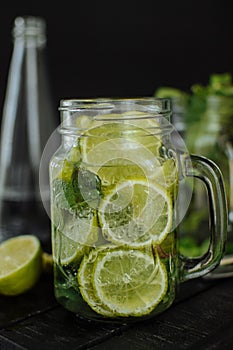 A glass of lemonade with sliced lime and lemon in a mug on a black background.