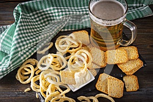 Glass of light beer with appetizer, cracker, onion rings and sauce, checkered green towel on a dark