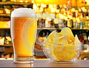 Glass of light beer and chips on bar counter in pub