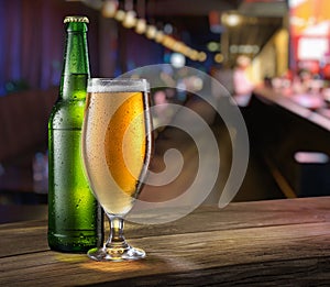 Glass of light beer and green beer bottle on the bar counter