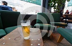 Glass of light beer inside bar or cafe with drinking people, old chairs and other vintage furniture.
