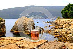 Glass of light beer near sea. Misted mug, pint of cold beer stands against background of blurred sea and mountain landscape in