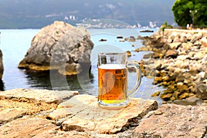 Glass of light beer near sea. Misted mug, pint of cold beer stands against background of blurred sea and mountain landscape in