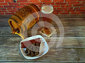 A glass of light beer, a plate with rye croutons with garlic and smoked Bavarian sausages, a wooden keg of beer stand on a wooden