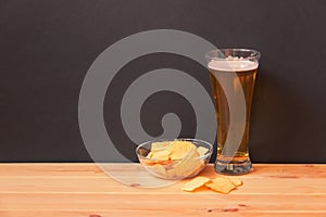 Glass of light  beer and potato chips on wooden table. View with copy space