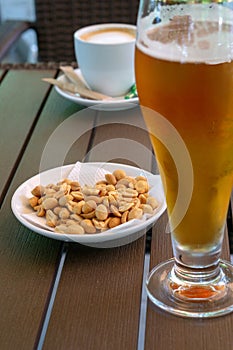 Glass with light beer, roasted peanuts and a cup of americano on a wooden table. Soft focus