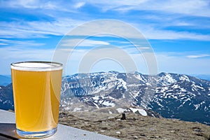 Glass of light beer with view of mountains. Beautiful view of rocks, forest and blue sky. Scenic mountain landscape