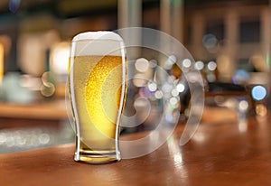 Glass with light beer on a wooden table against the backdrop of a dark pub. Beer vintage concept