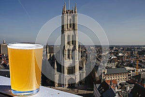 Glass of light Belgian beer against view of big cathedral in Ghent