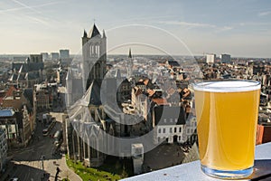 Glass of light Belgian beer against view of big cathedral in Ghent, Belgium. View from above of Ghent