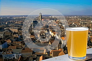 Glass of light Belgian beer with panoramic view from above of old town and big cathedral in Ghent, Belgium. View from above of