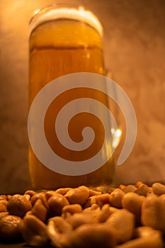 Glass of light cold frothy beer, nuts on an old wooden table.