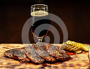 Glass of light foam beer with meat appetizer on a wooden table on a black background