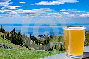 Glass of light wheat beer against mountains background. View of blue sea and green valley in the mountains