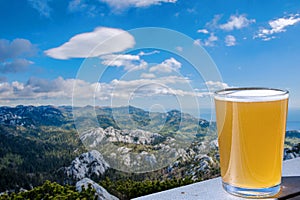 Glass of light wheat beer against mountains background. View of green valley in the mountains