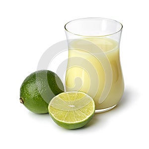 Glass with lime juice and green lime in front on white background