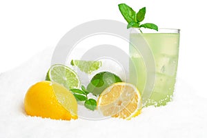 Glass of lime juice,lemons,ice cubes on snow on white