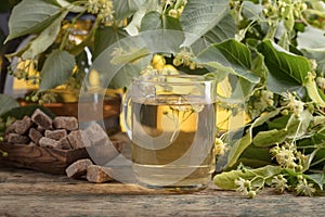 Glass of linden tea with brown sugar and flowers on wooden table