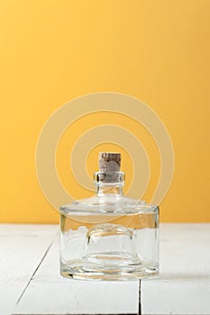 A glass low bottle with a natural cork on a white-and-yellow background