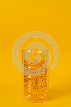 A glass of mango drink with basil seeds on a yellow background