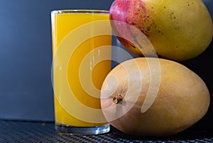 Glass of mango juice with natural fruits on dark background