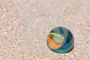 Glass marble with colored interior resting on the sand