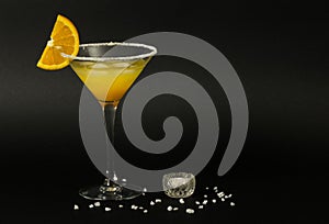 Glass of margarita cocktail with salty rim and slice of orange on black background.