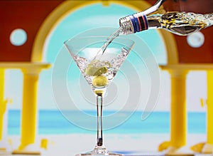 Glass with martini and green olives and bottle on tropical background.