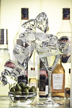 Pieces of ice, glass bowl with green olives and a glass of martini