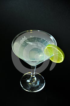 A glass of martini with ice and a slice of lime on the edge, composition on a black background