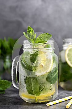 Glass mason jar of ice tea with fresh mint, lemon and paper straw on dark background. Summer healthy cold drink. Alternative