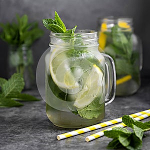 Glass mason jar of ice tea with fresh mint, lemon and paper straw on dark background. Summer healthy cold drink. Alternative