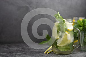 Glass mason jar of ice tea with fresh mint, lemon and paper straw on dark background. Summer healthy cold drink. Copy space