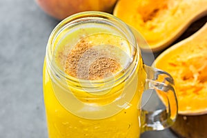 Glass mason jar with raw pumpkin butternut squash smoothie with peaches, bananas, cinnamon, spices. Ingredients on dark stone tabl