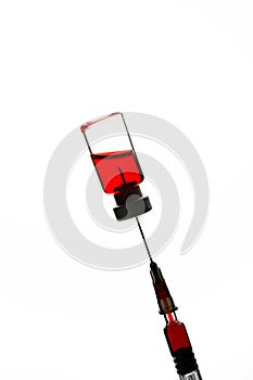 Glass medical ampoule for vaccination with red liquid and disposable syringe on a white background