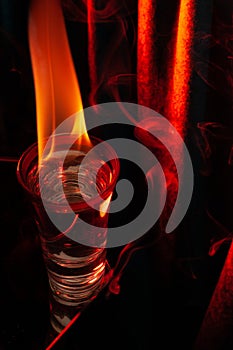 Glass of Mexican tequila, vodka with burning liquid. on red background. Glass of vodka on black with flames.
