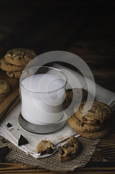 Glass of milk with appetizing delicious sweet homemade chocolate chip on dark vintage wooden table. Tasty dessert for breakfast wi