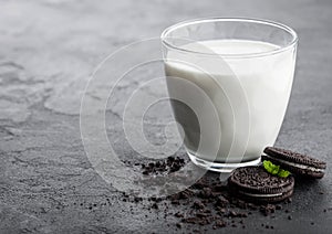 Glass of milk and black sandwich cookies on black stone kitchen table background. Space for text