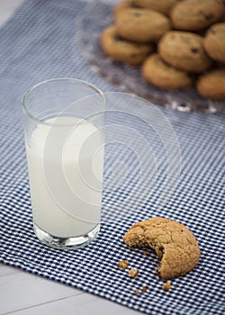 A glass of milk and a cookie with a bite taken out of it sit on