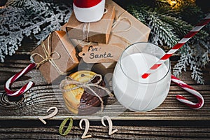 A glass of milk, cookies, santa hat, numbers 2022 and gifts on the table.