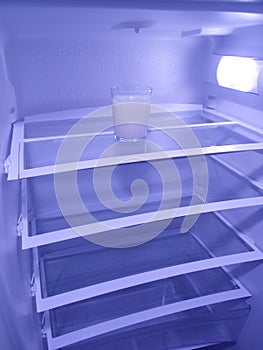 Glass of milk in empty refrigerator