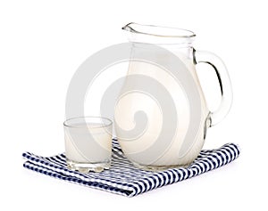 A glass of milk and a milk jug on plaid tablecloth