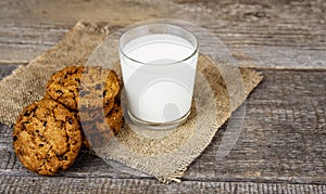 Glass with milk and oatmeal cookies on burlap on a wooden background